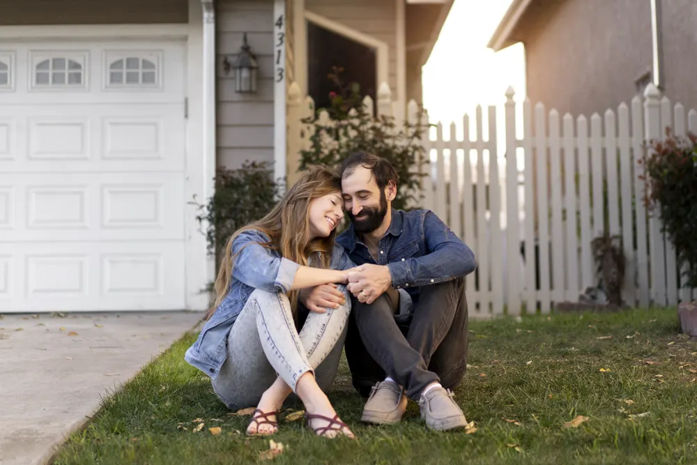 A couple sitting together on the front lawn of their home