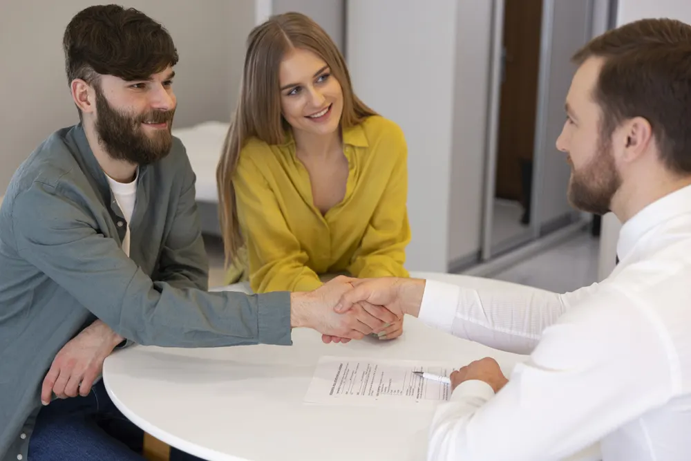 A couple shaking hands with their BBS broker across the table