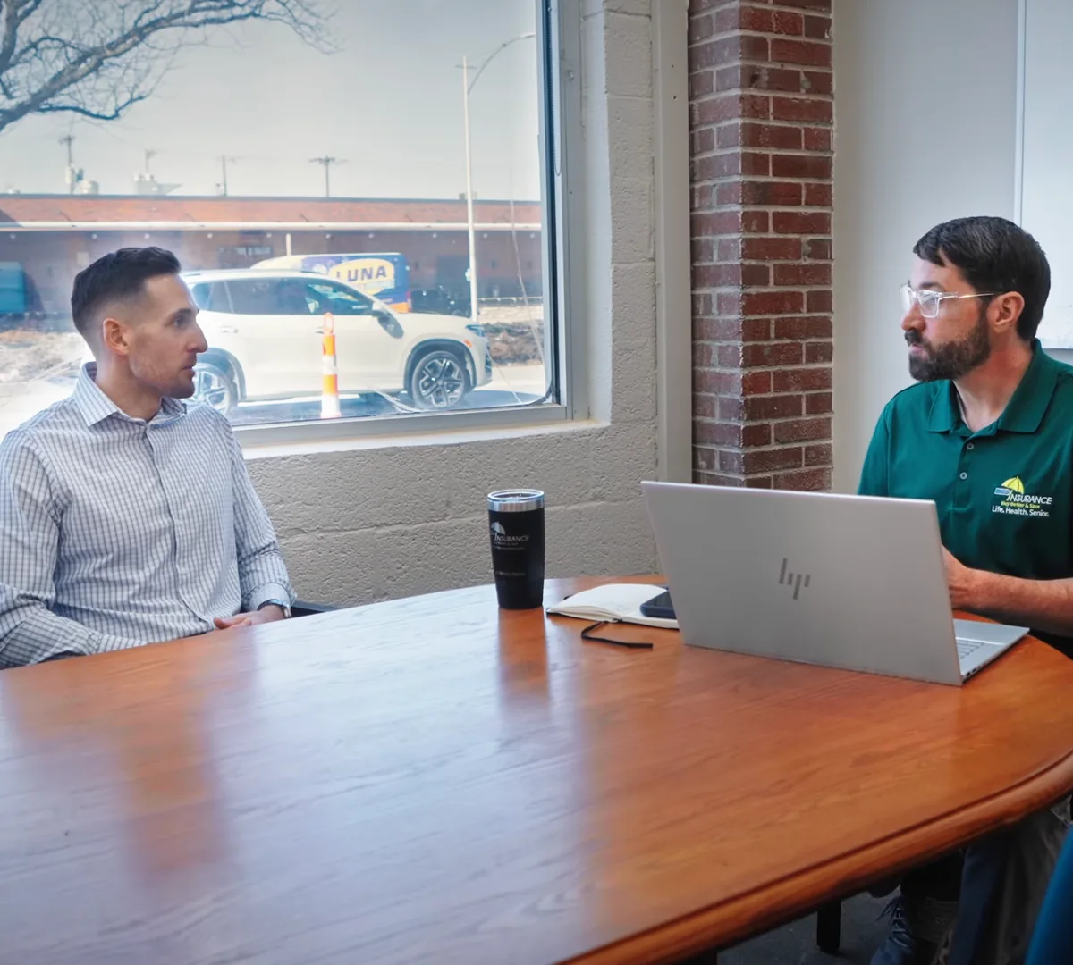 Two BBS Insurance brokers at the meeting table inside the North Kansas City office, a laptop open between them